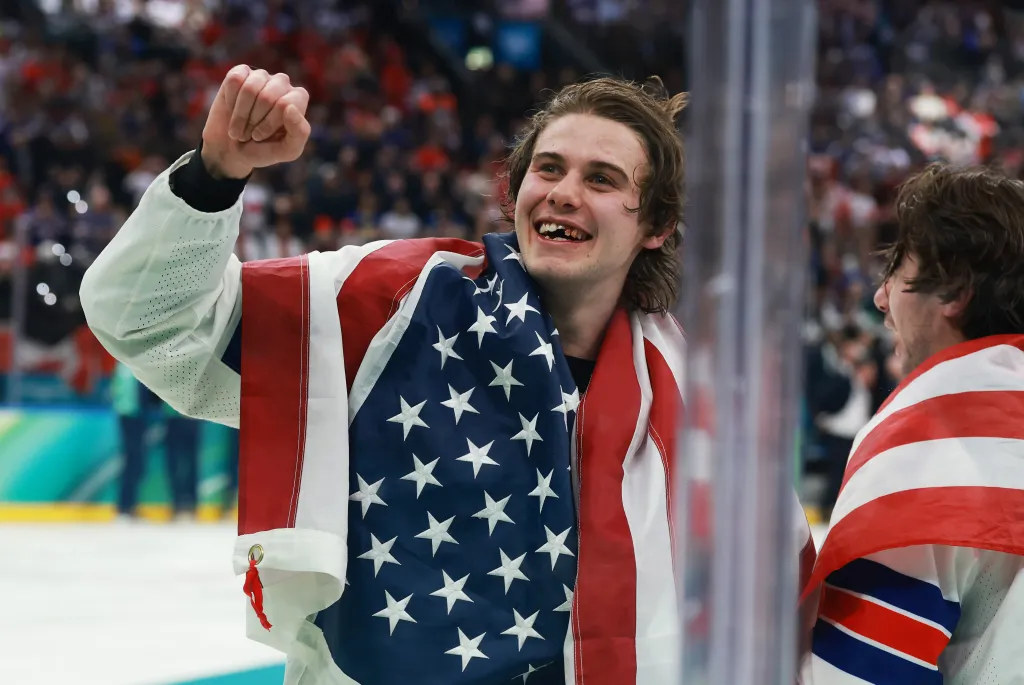 Jack Hughes of Team United States, draped in an American flag, celebrates after winning the gold medal in ice hockey.