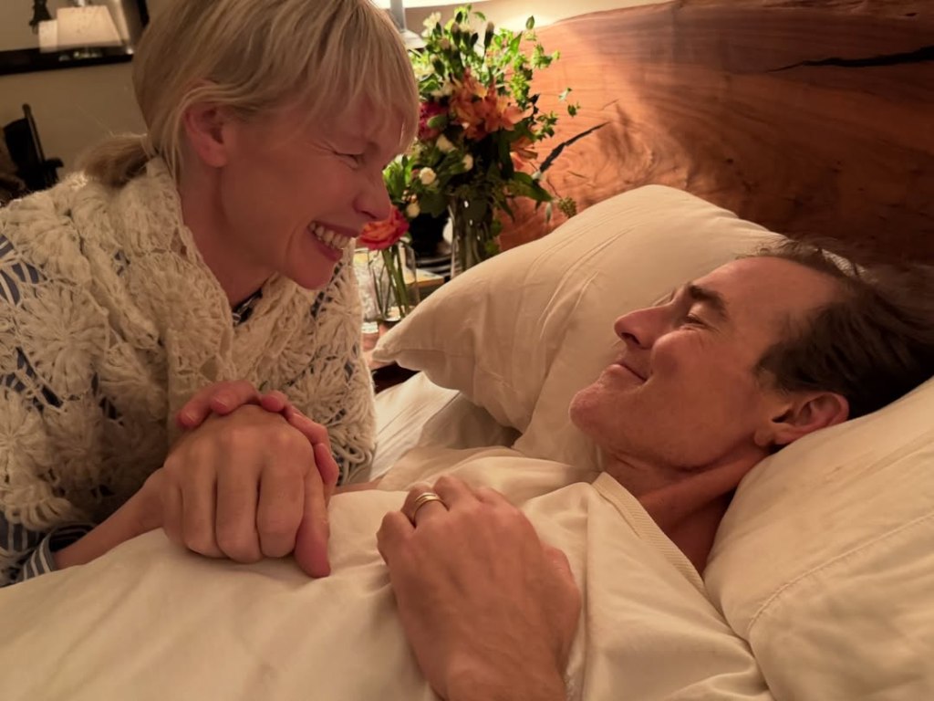 Erin Fetherston holding hands with James Van Der Beek, who is lying in bed.