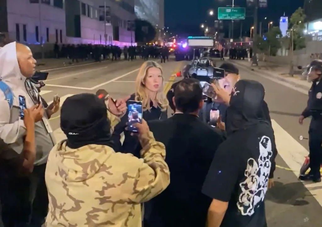 Fox 11 News crew being heckled by a crowd at an unlawful assembly outside a federal building.