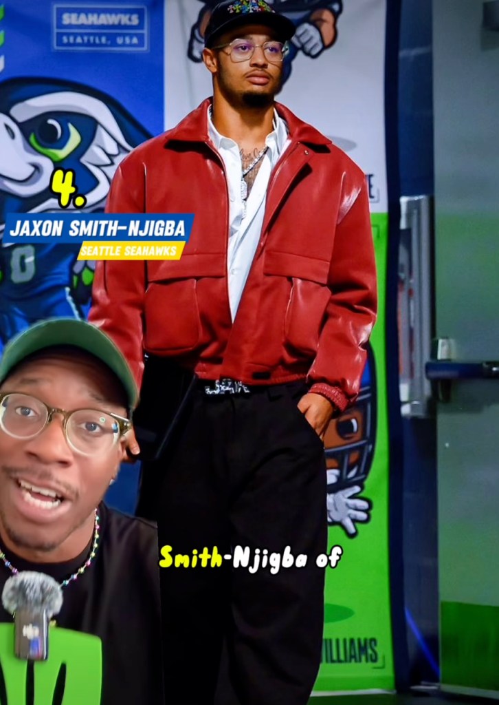 A man wearing a red jacket and black pants, with an inset image of another man talking.