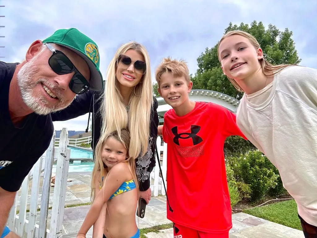 Family selfie of Jessica Simpson, Eric Johnson, and their three children by a pool.