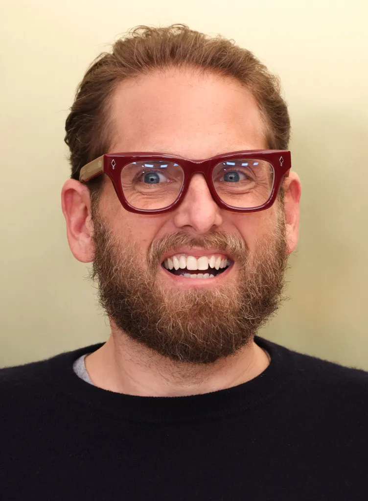 Jonah Hill smiling and wearing red glasses.