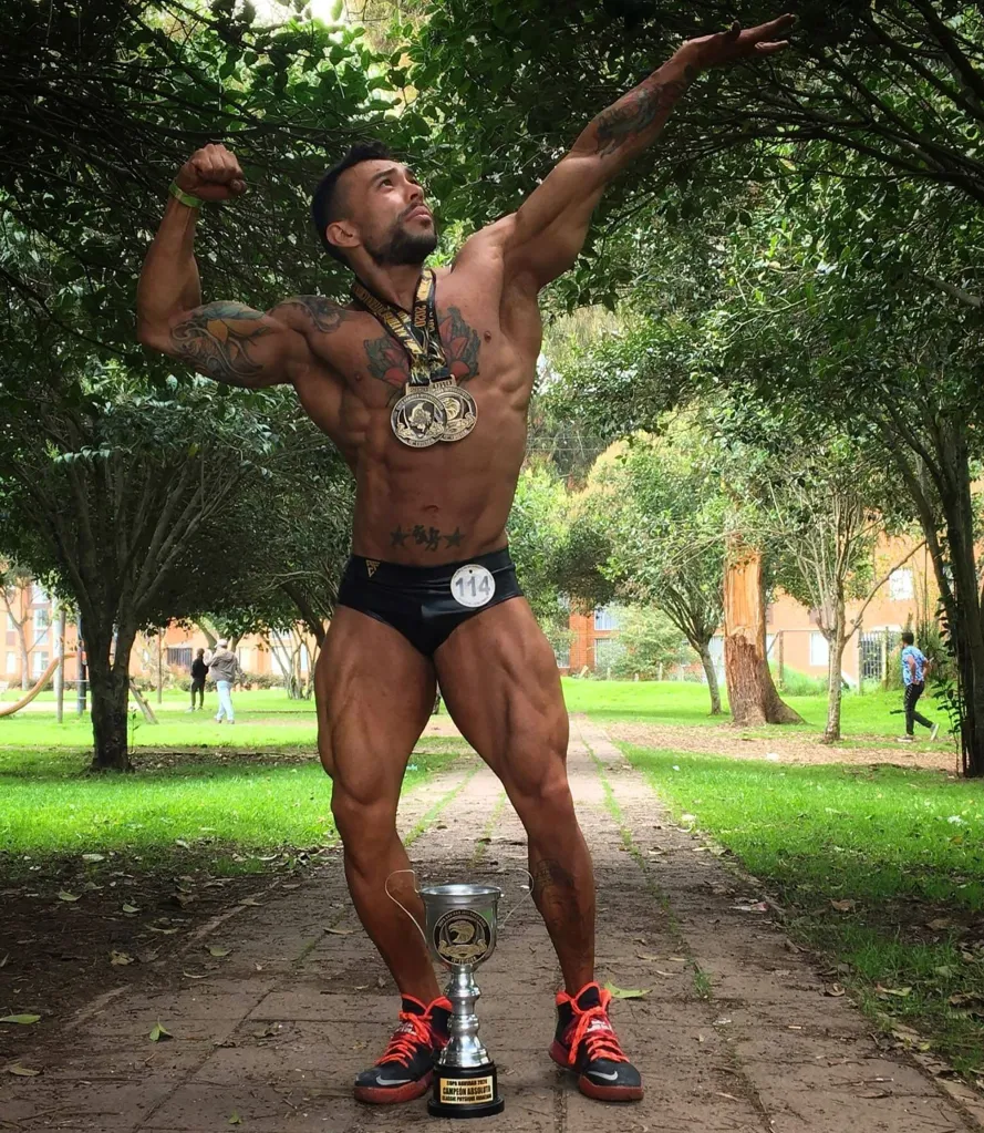 Juan Sebastian Anzola Quintero poses in black briefs with a medal around his neck and a trophy at his feet.