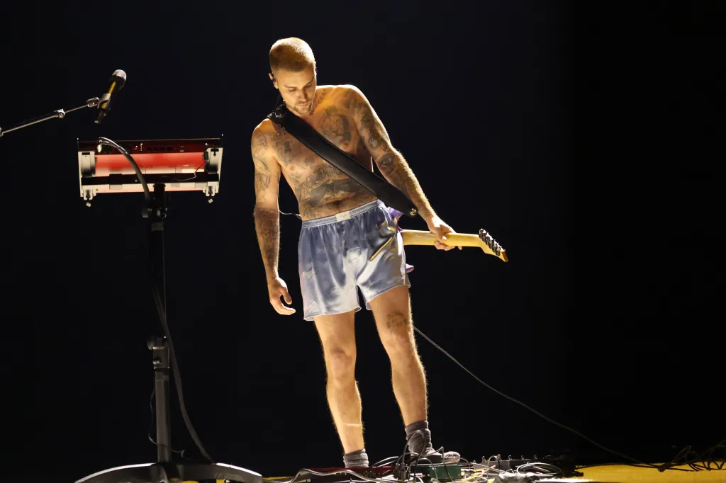 Justin Bieber performs shirtless in blue shorts with a guitar at the 68th GRAMMY Awards.