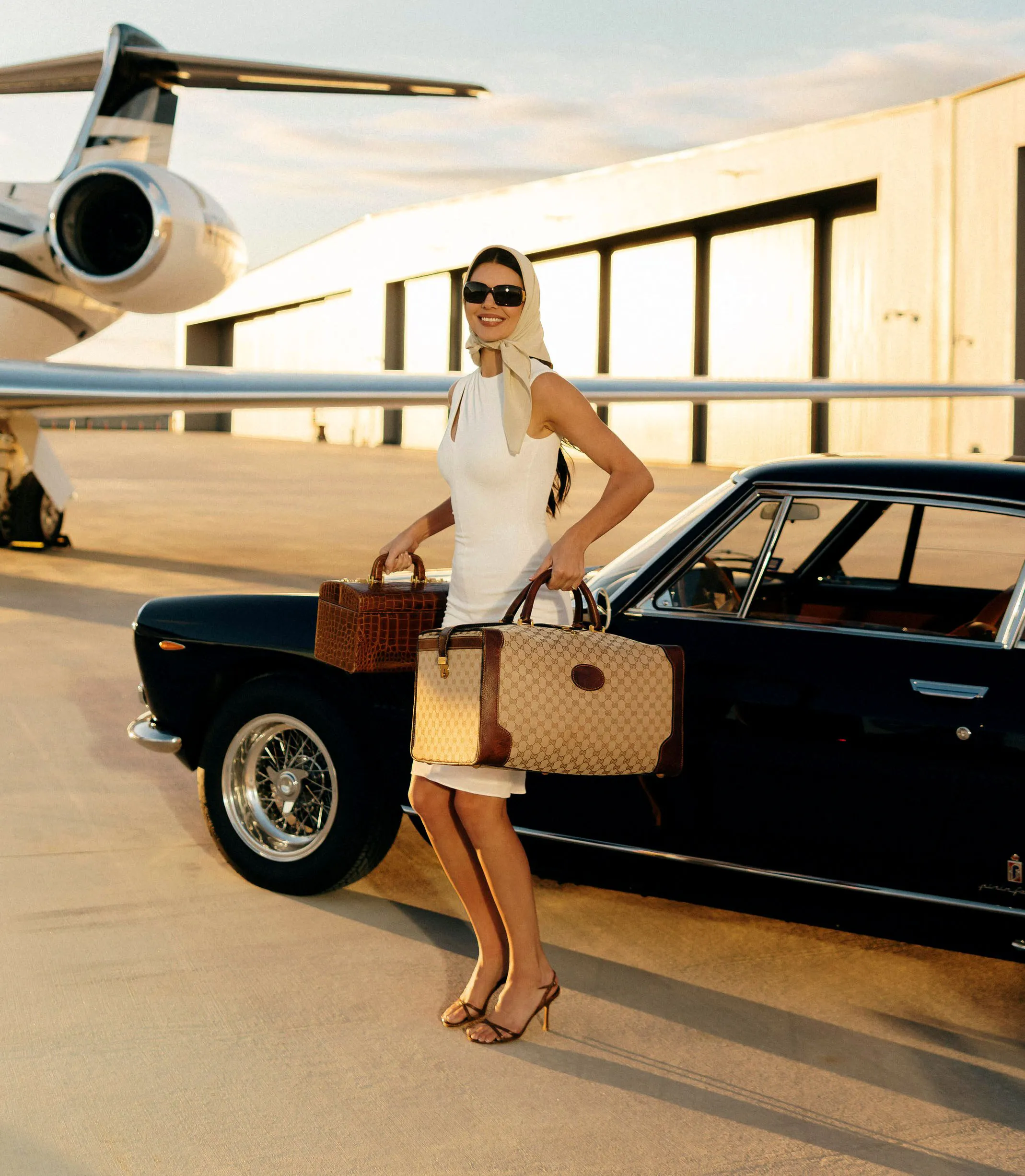 Kendall Jenner poses with two handbags next to a vintage car and private jet.