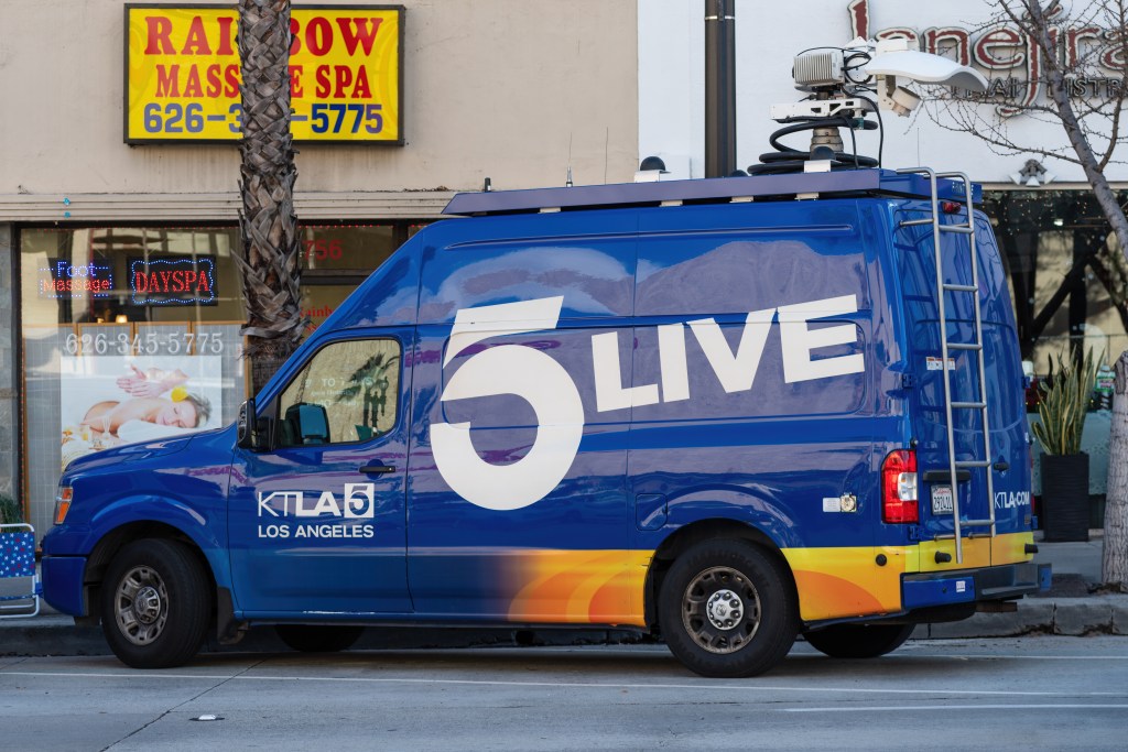 A blue KTLA 5 News van with a satellite dish on its roof, parked on a street in Pasadena.