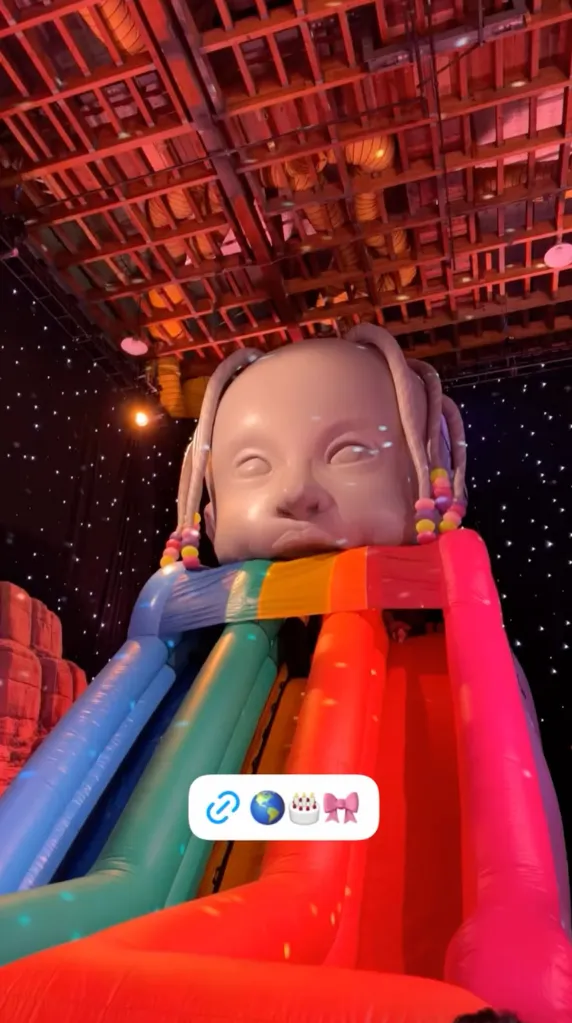 An inflatable slide decorated with a giant head of a baby wearing pigtails with colorful beads.