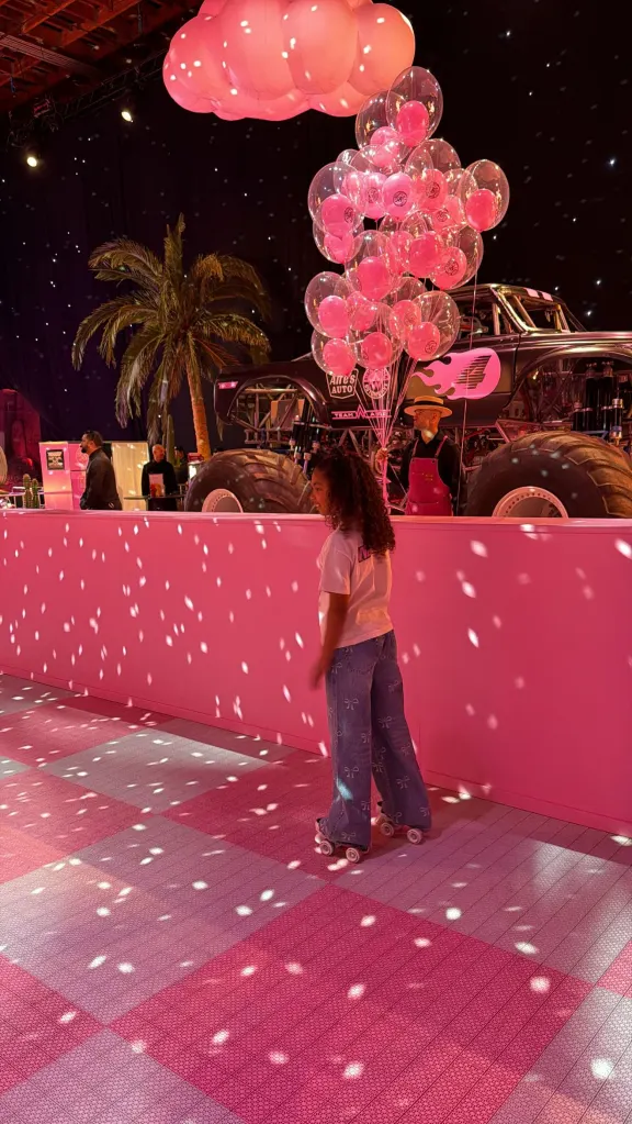 Stormi Webster rollerskating on a pink and white checkered floor, with pink balloons and a monster truck in the background.