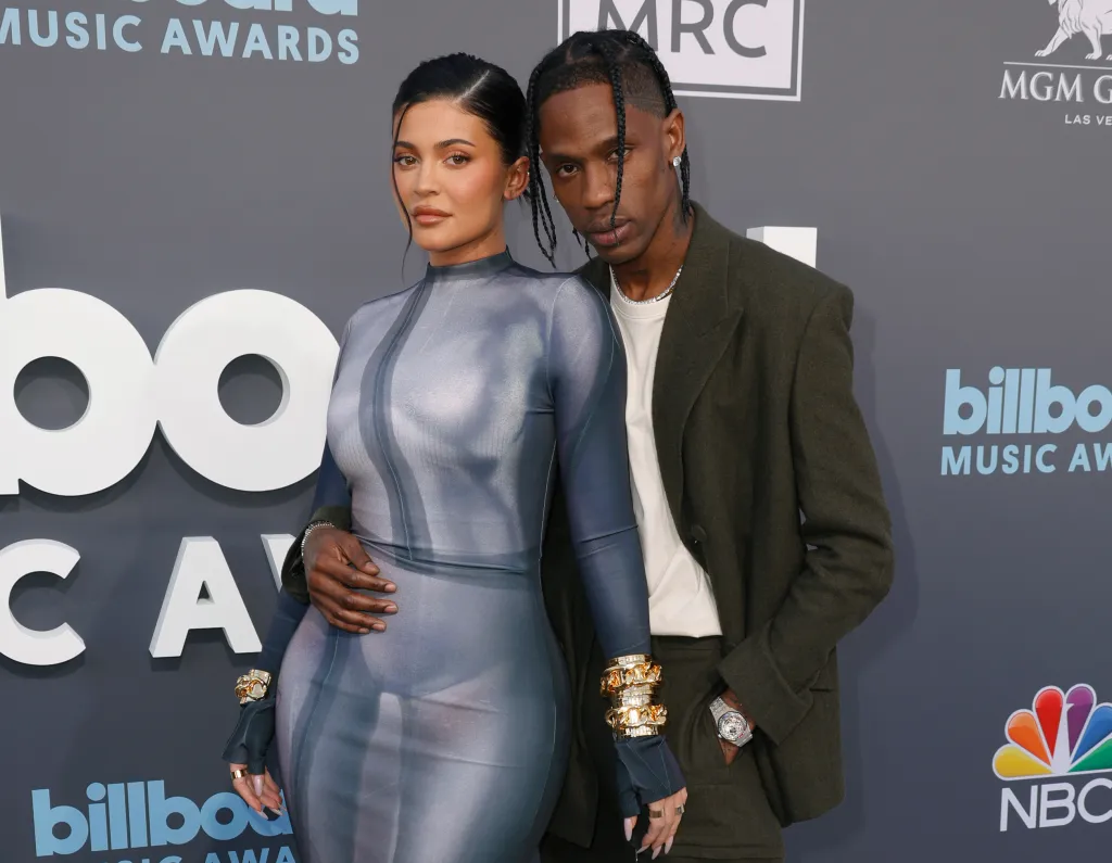Kylie Jenner in a sheer blue bodycon dress and Travis Scott in a dark green suit attend the 2022 Billboard Music Awards.