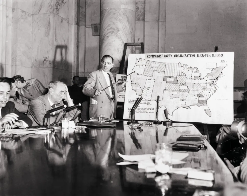 Senator Joseph McCarthy testifying on Communist Party organization in the US with a map at a hearing.