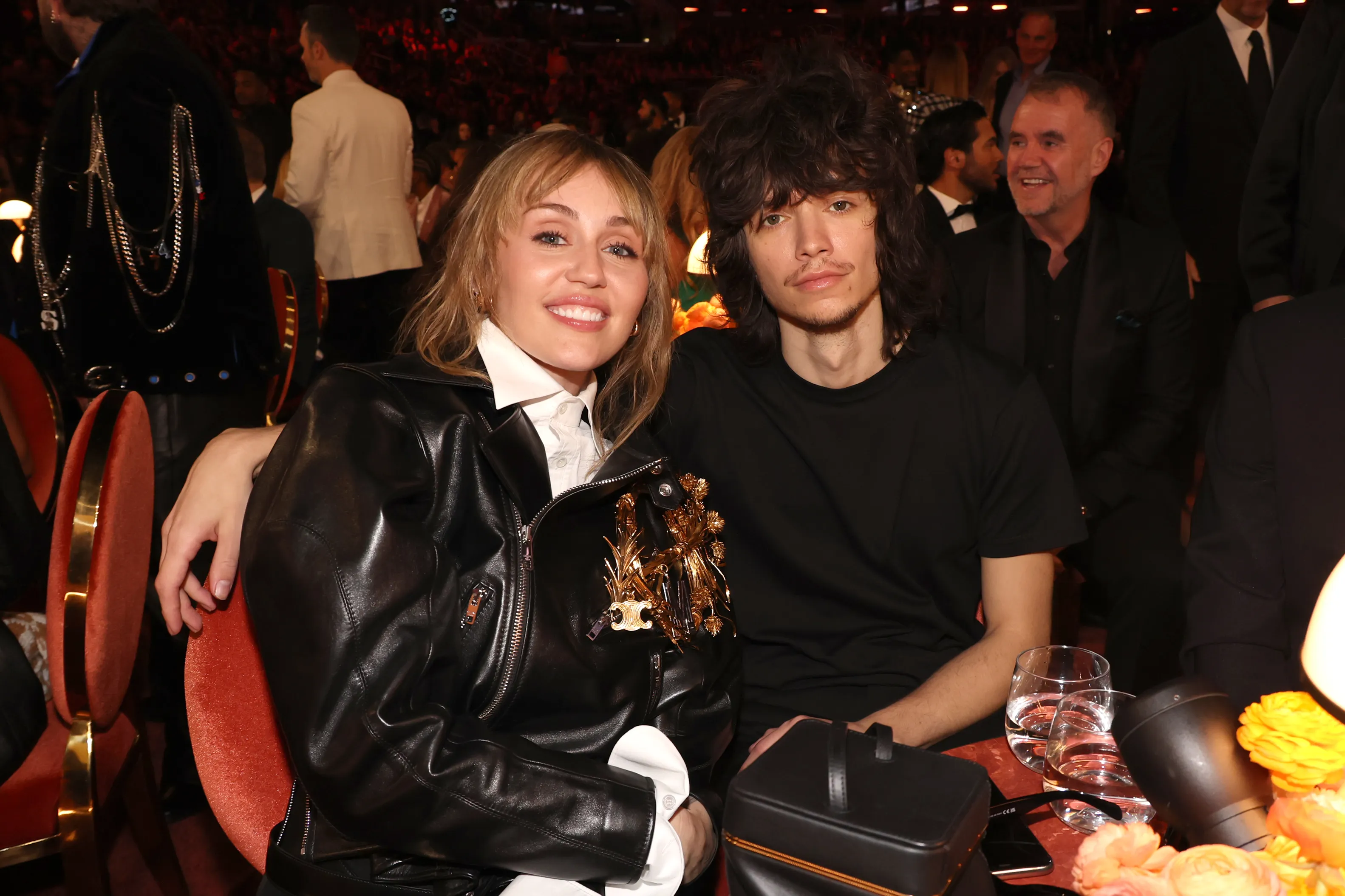 Miley Cyrus in a black leather jacket with a gold brooch and Maxx Morando in a black t-shirt, both seated at the 68th Grammy Awards.