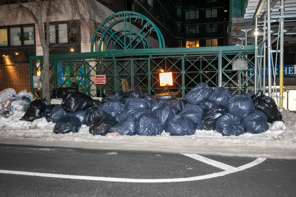 Large piles of trash bags on a snowy sidewalk near 909 3rd Ave in Midtown, Manhattan.