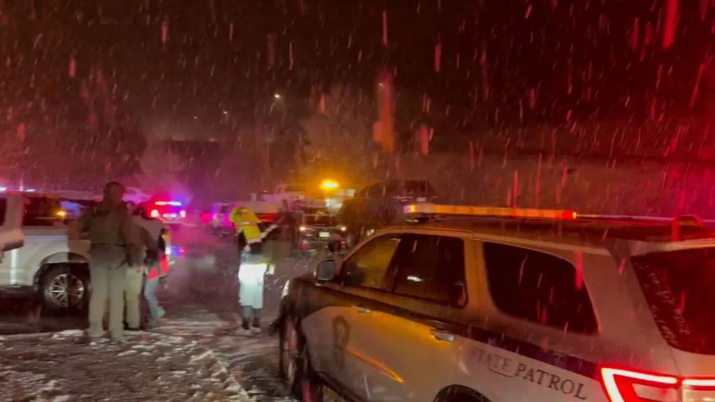 Snowy scene of a multi-car crash on a Colorado interstate with State Patrol and emergency lights flashing.