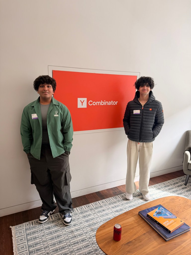 Aayam Bansal (left) and Ishaan Gangwani (right) stand in front of a red Y Combinator sign.
