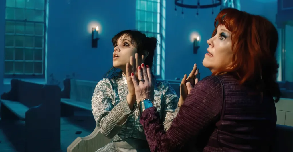 Jenna Ortega and Catherine O'Hara looking up in an eerie blue room.