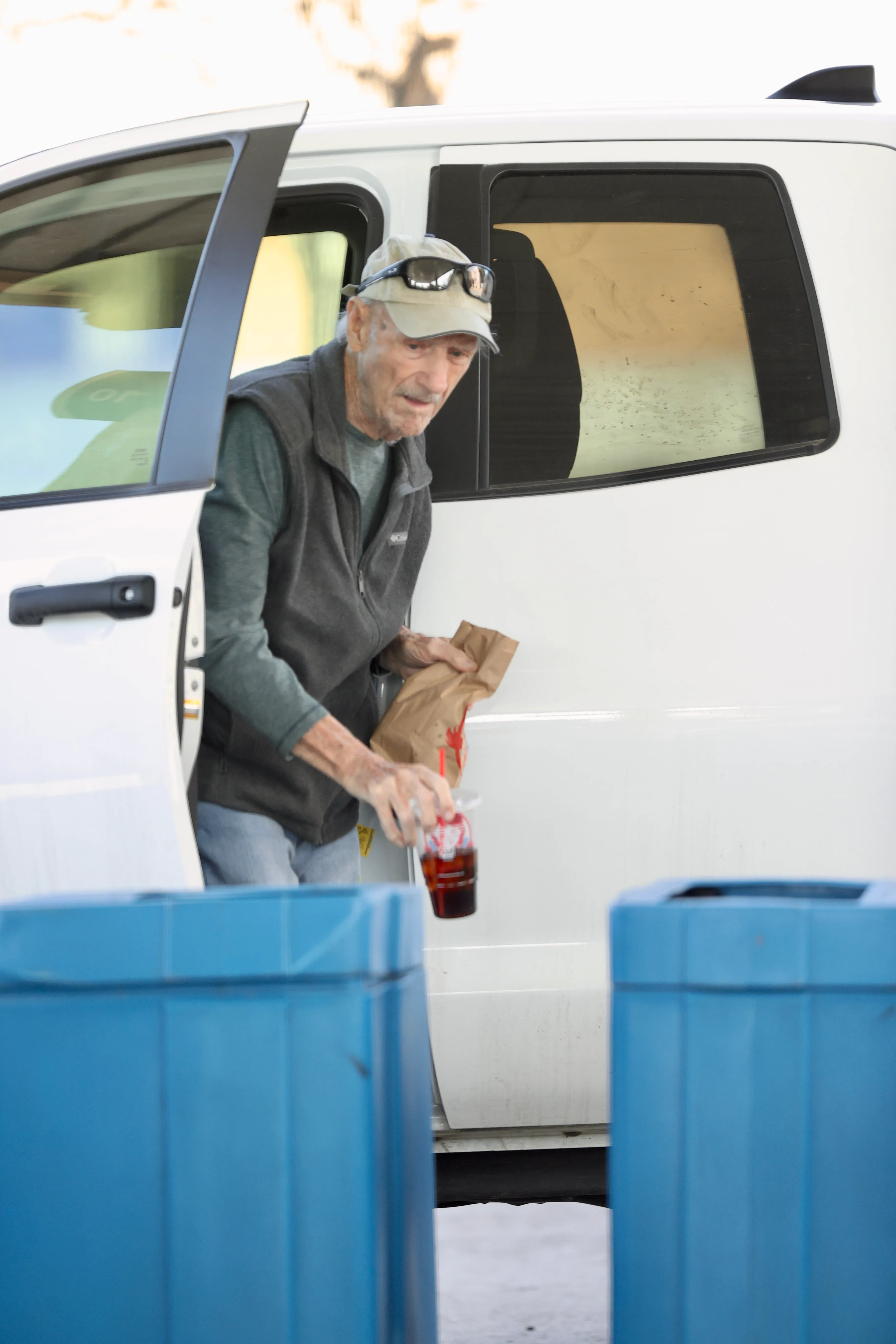 Gene Hackman exiting a white vehicle with a fast-food drink and bag.