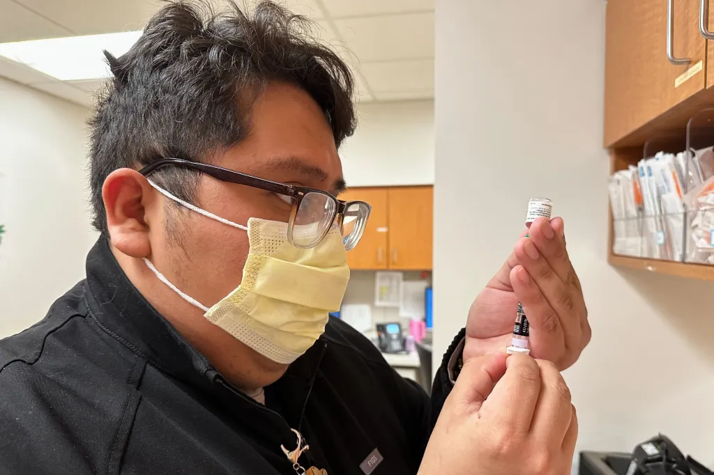 A nurse in a mask and glasses prepares a measles, mumps, and rubella vaccine.