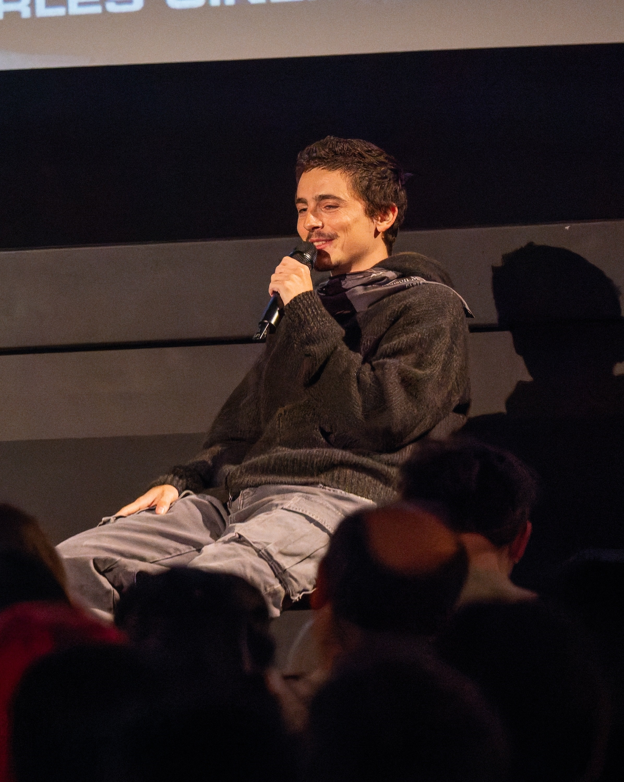 Timothée Chalamet smiling and holding a microphone at a fan event in London.