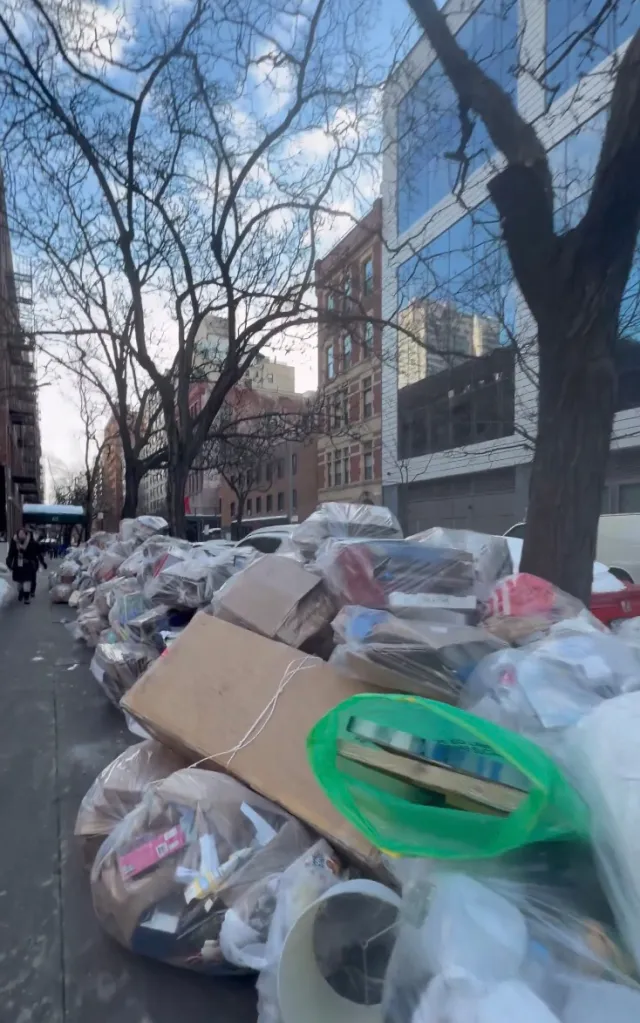 A large pile of garbage bags and cardboard boxes lining a sidewalk in an urban setting.