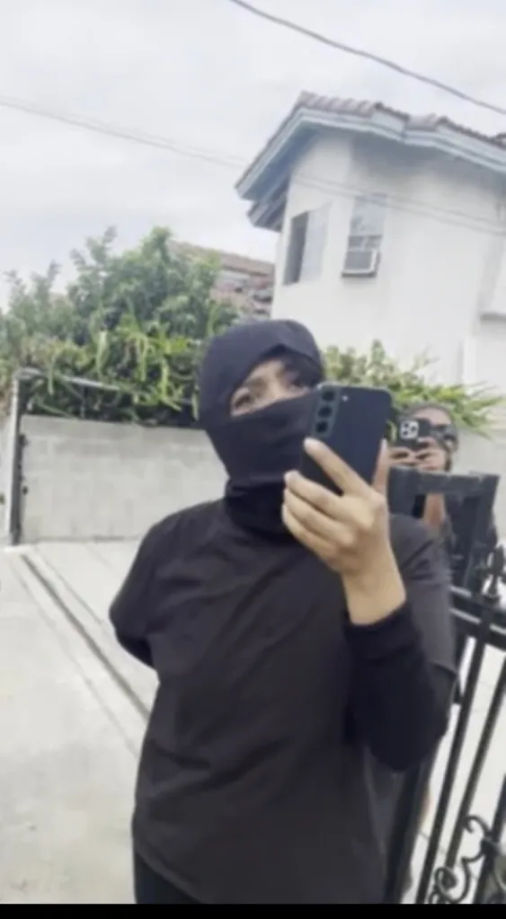A person in a black ski mask taking a selfie with a phone.
