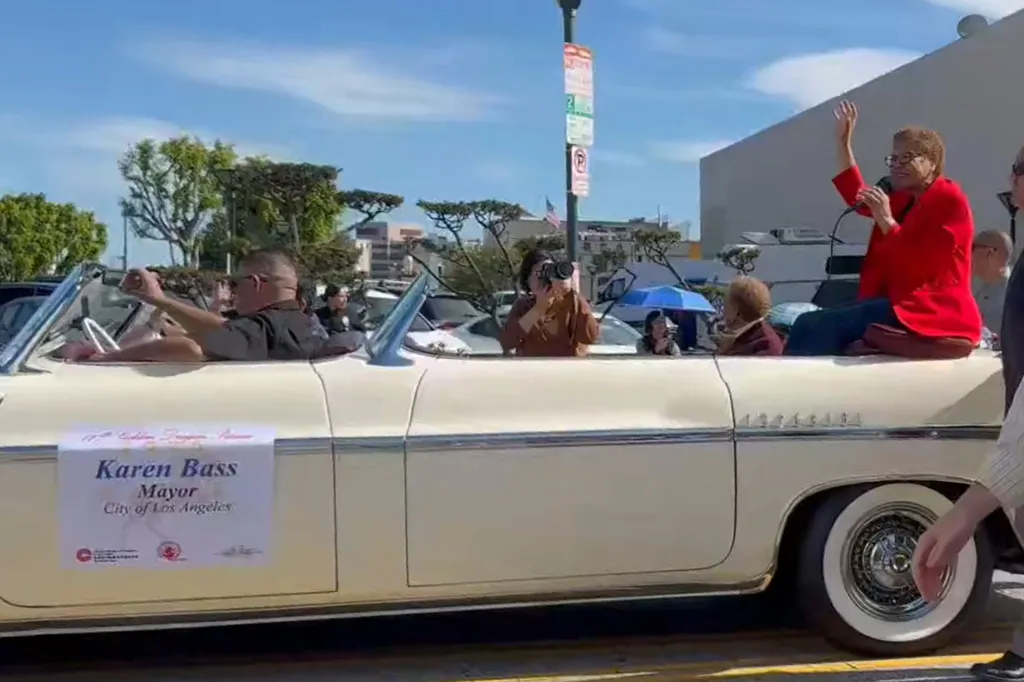 Los Angeles Mayor Karen Bass waving from the back of a convertible car in a parade.