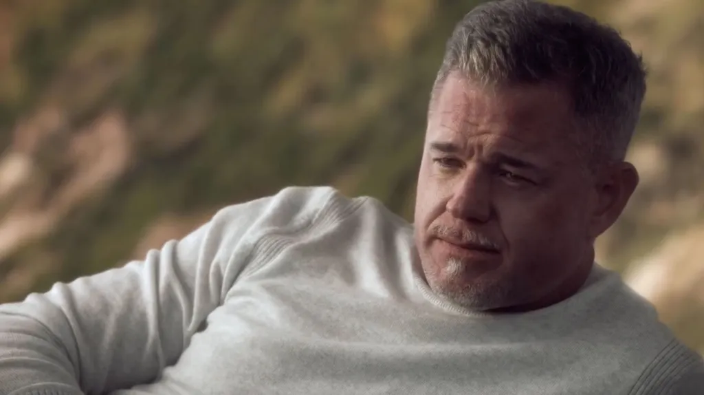 Eric Dane, a man with graying hair and beard, wearing a light-colored sweater, looks into the distance.
