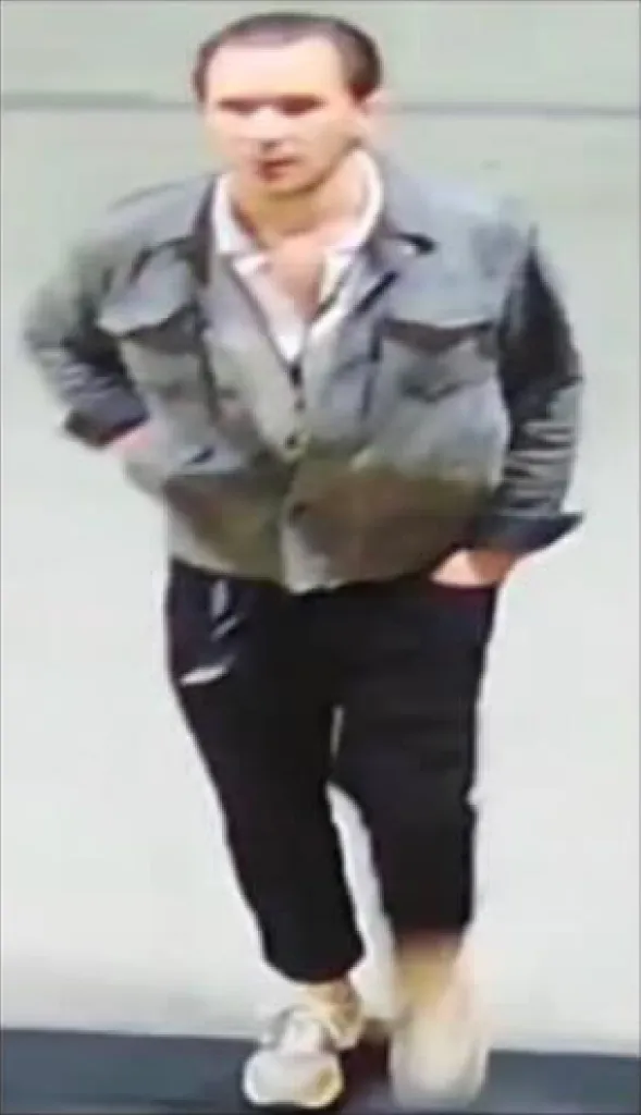 Mugshot of a man with short brown hair, wearing a gray jacket, white shirt, and black pants.