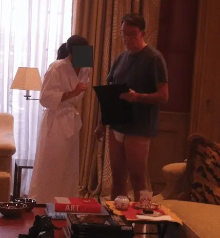 Peter Mandelson in underwear, holding a folder, with a person in a robe.