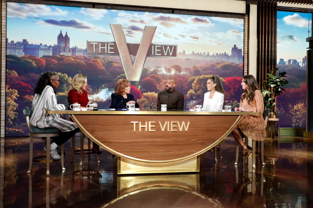 The cast of The View and guest Marlon Wayans sit behind a crescent-shaped desk.