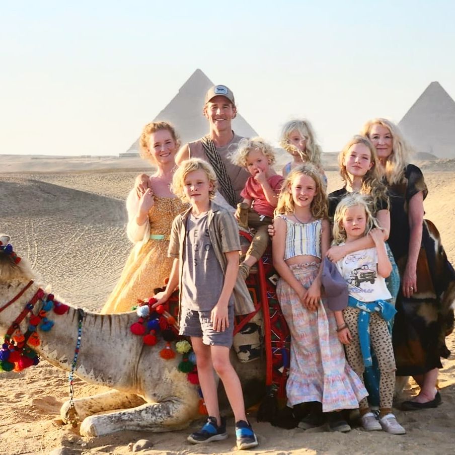 James Van Der Beek, his wife Kimberly, and their six children posing with a camel and the pyramids in the background.