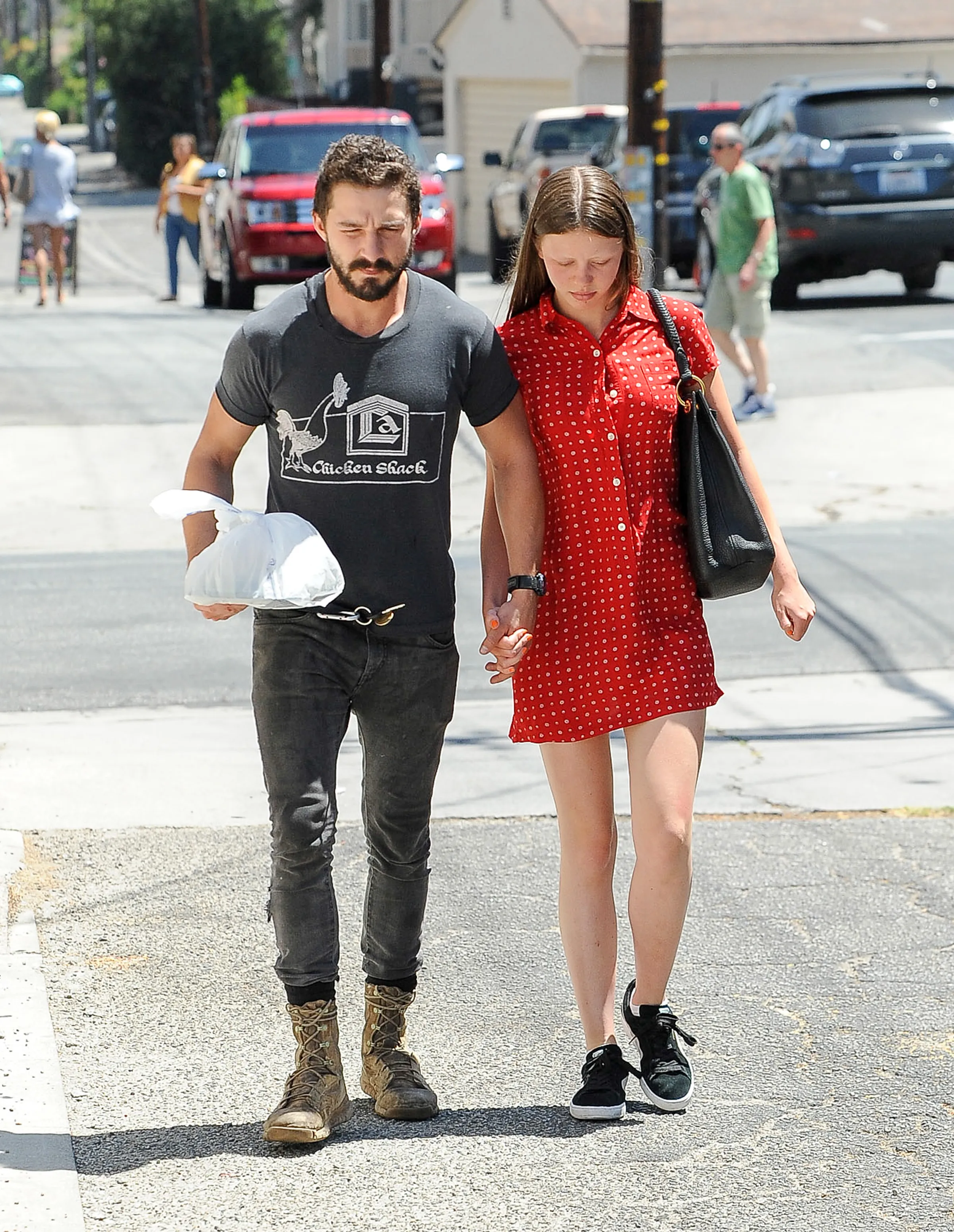 Shia LaBeouf and Mia Goth holding hands and walking down a street.