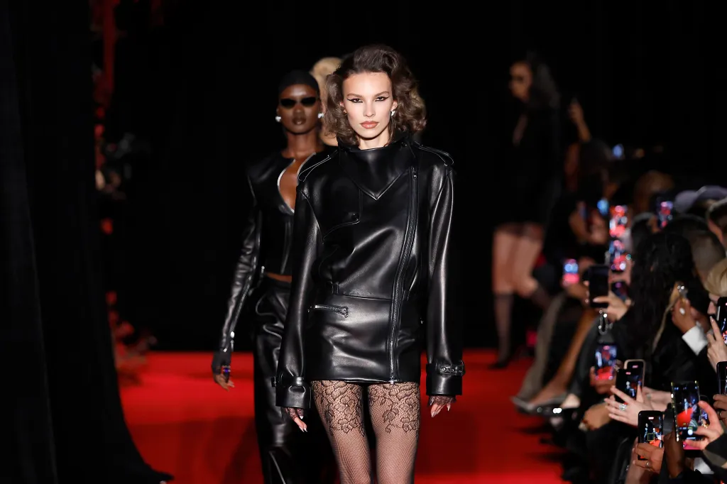 A model wearing a black leather jacket and sheer patterned tights walks the runway at the LaQuan Smith show.