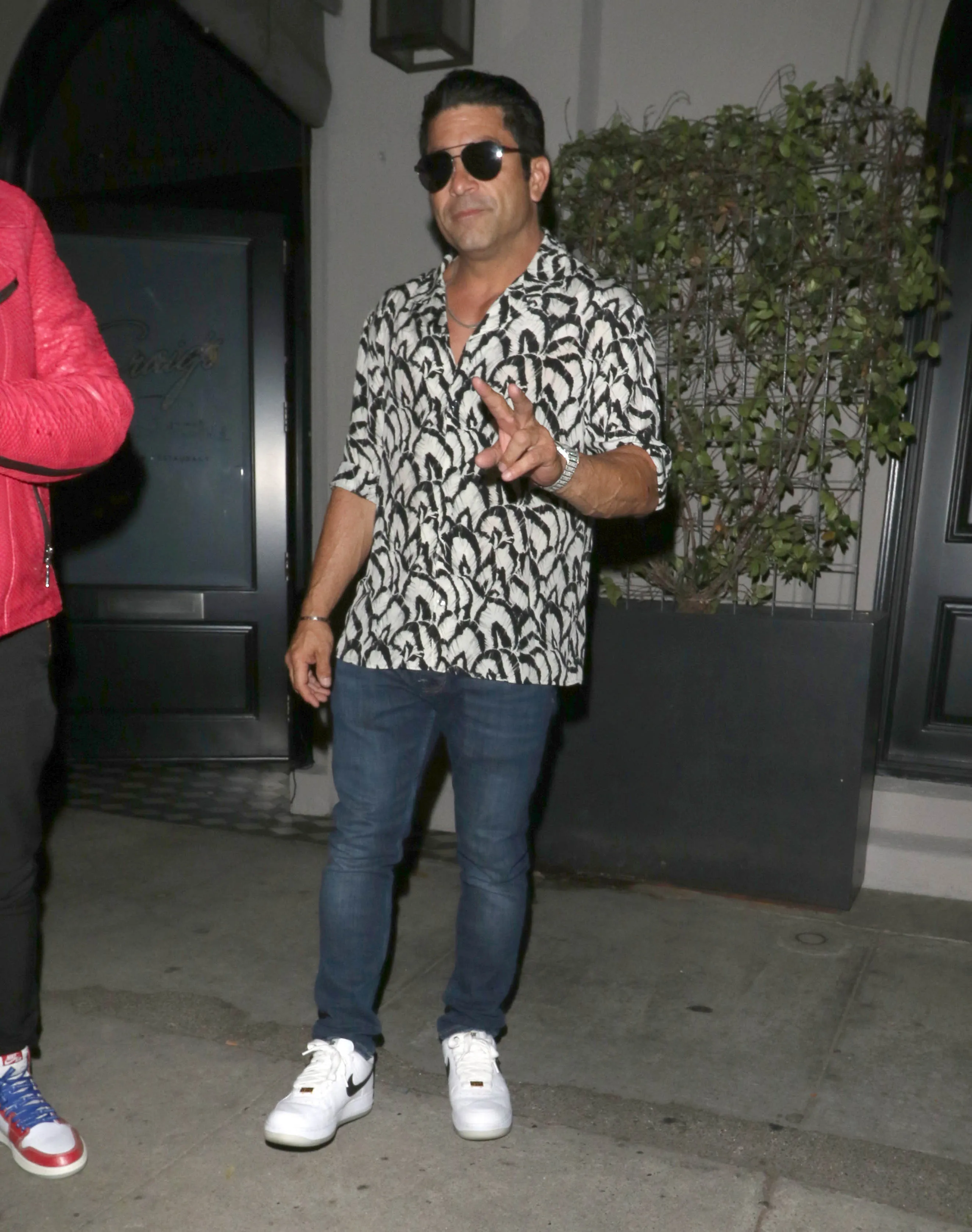Monty Lopez posing in sunglasses and a patterned short-sleeved shirt with jeans and white sneakers.