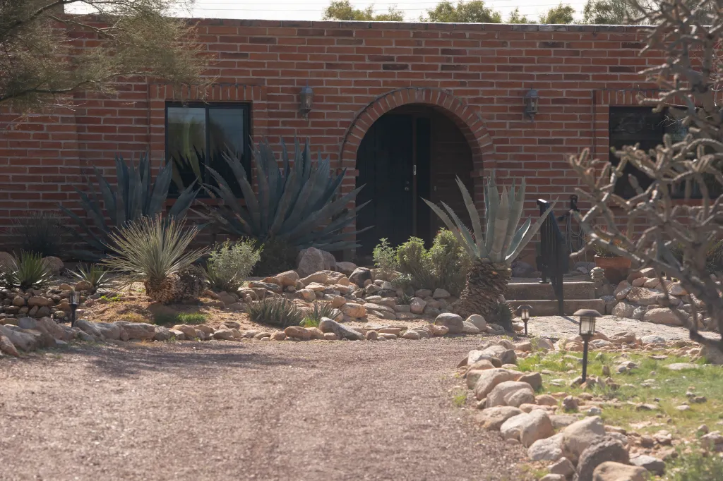 Nancy Guthrie's house in Tucson, Arizona, showing a brick facade with a dark arched entrance and xeriscaped front yard.