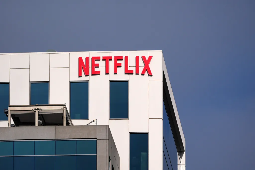 The Netflix logo in red letters on top of a white and gray building against a blue sky.