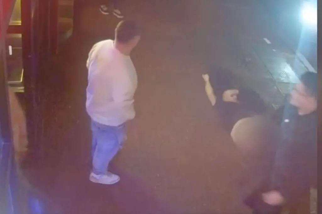 Still image from security video showing a man in a white shirt standing over another man lying on the ground.