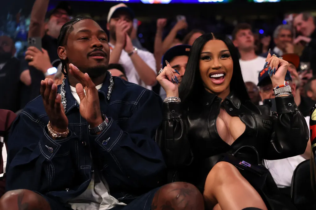 NFL player Stefon Diggs and rapper Cardi B applauding courtside at a basketball game.
