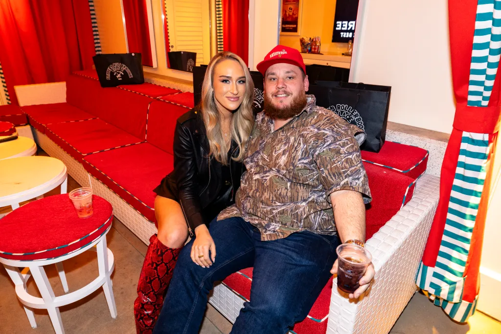 Nicole Combs and Luke Combs sitting on a red and white striped couch with black gift bags in the background.