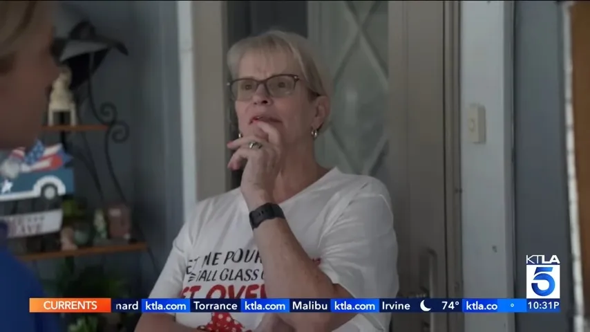 A woman in glasses wearing a white T-shirt with text printed on it talks to someone off-camera.