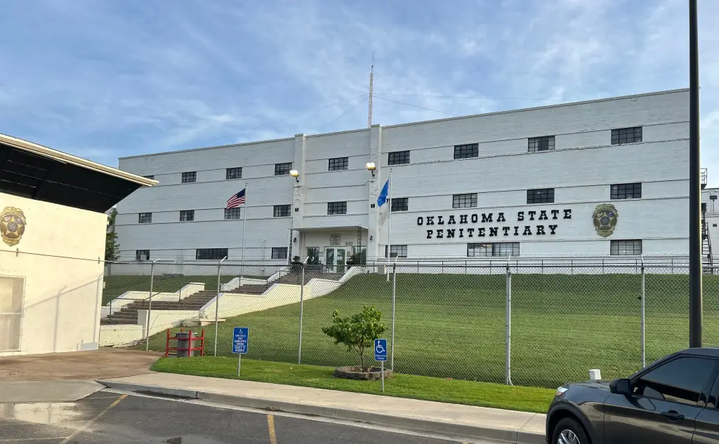 The Oklahoma State Penitentiary in McAlester, a large white building with an American flag and the penitentiary's name on its facade.