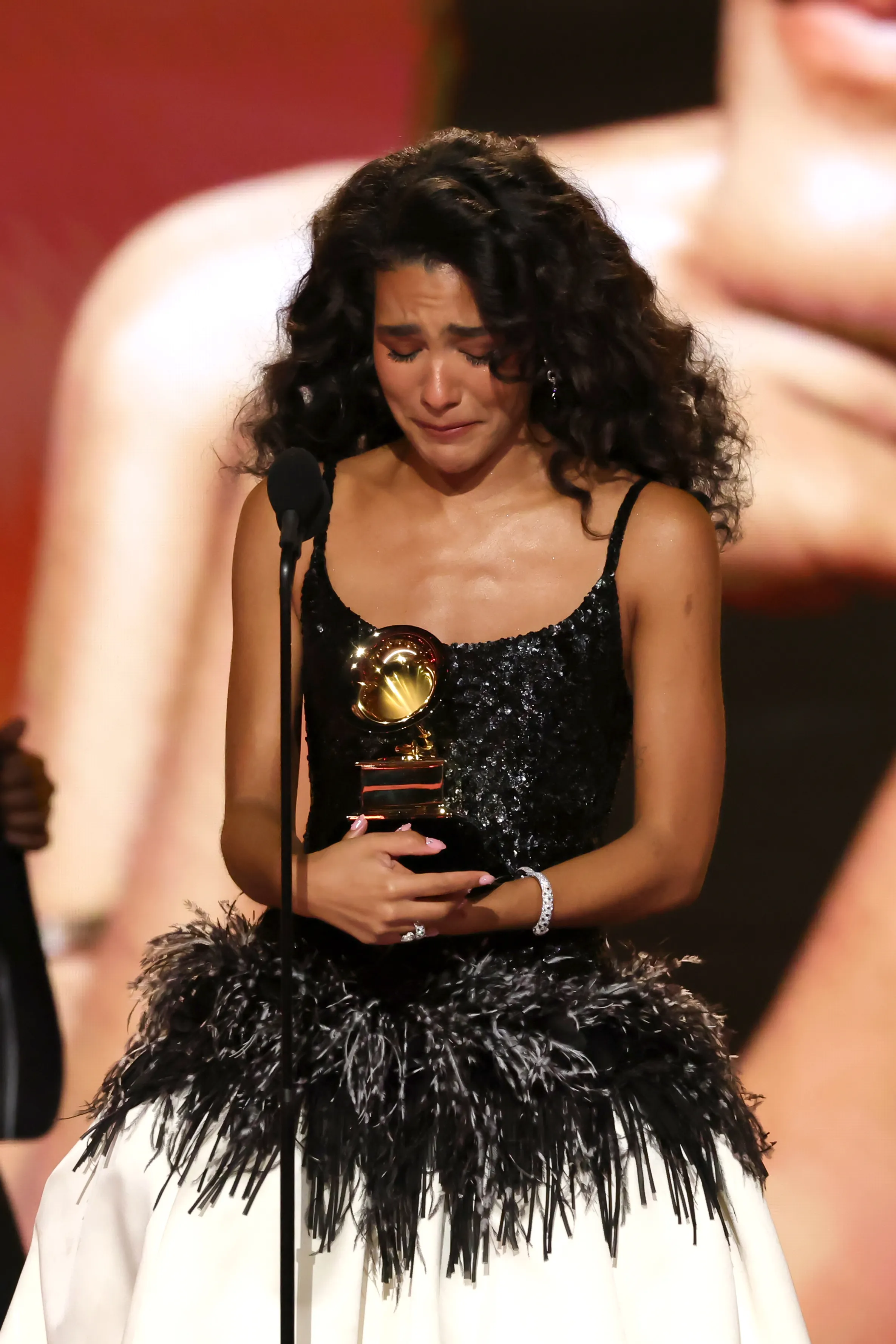 Olivia Dean onstage, crying and looking at the gramophone after her winning Best New Artist at the 2026 Grammys
