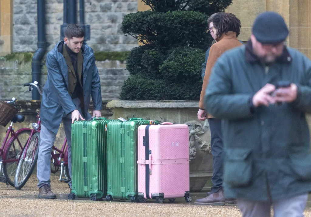 A man arranging two green suitcases and one pink suitcase, with 