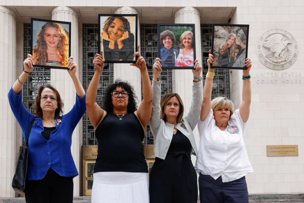 Four women hold up framed photos of young people outside a courthouse.