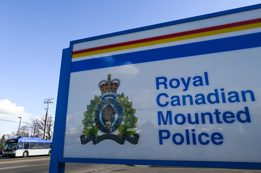 Sign for the Royal Canadian Mounted Police with its crest, a bus and a utility pole in the background.