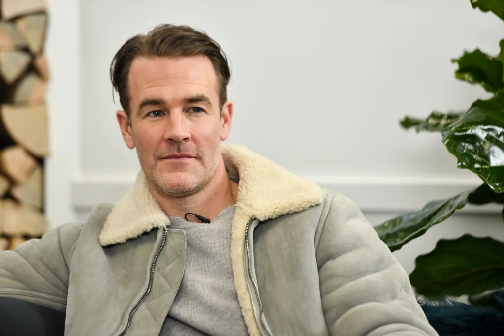 James Van Der Beek sitting, wearing a gray jacket with a sheepskin collar.