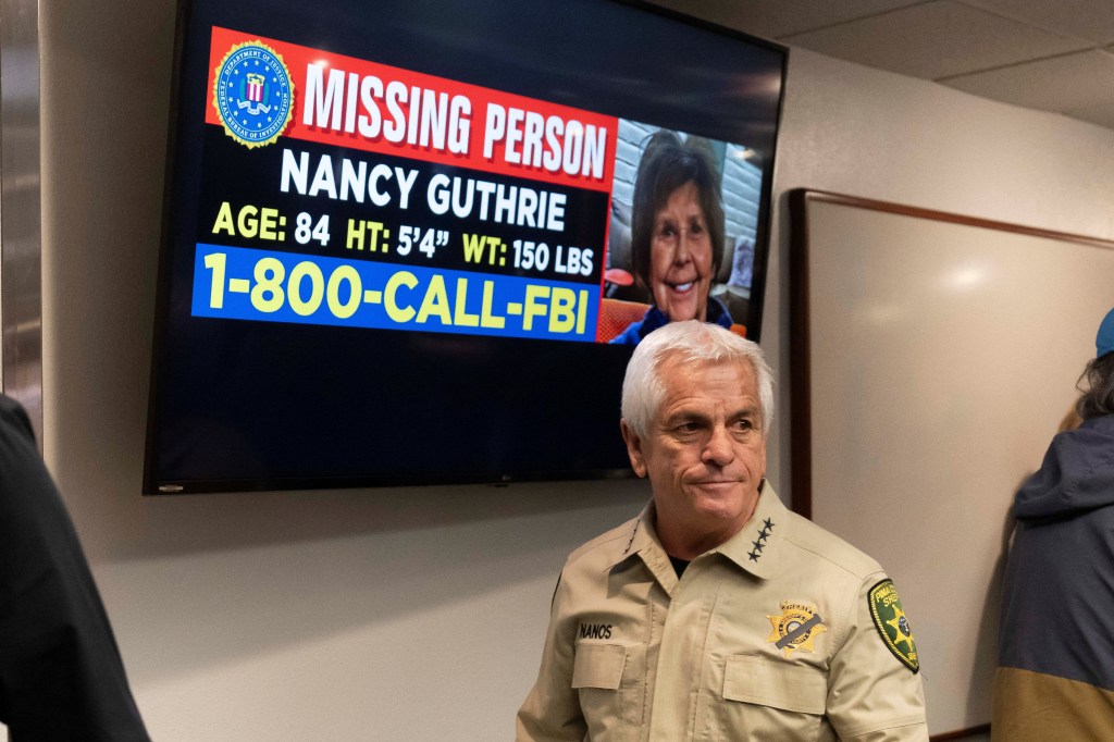 Pima County Sheriff Chris Nanos stands in front of a monitor displaying a missing person poster for Nancy Guthrie.