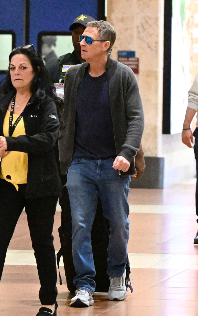 Michael Feldman, Savannah Guthrie's husband, walks through a Florida airport wearing blue jeans and a dark grey jacket, accompanied by other people.