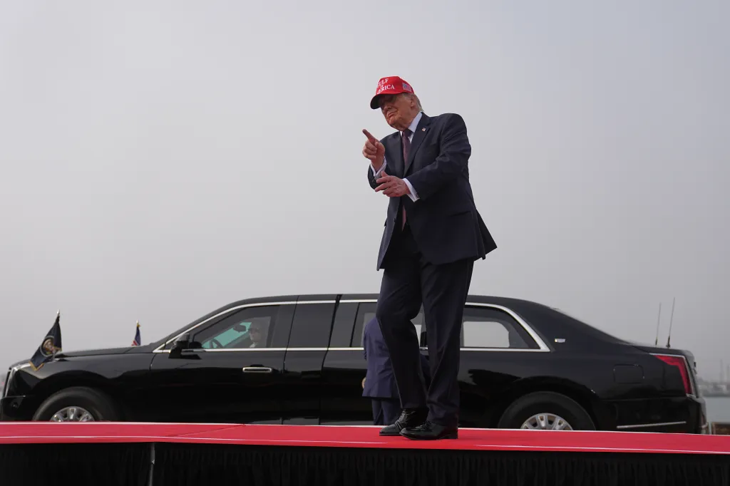 President Donald Trump gestures while speaking in front of a black limousine.