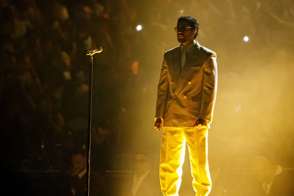 Bad Bunny performing on stage in a light suit.