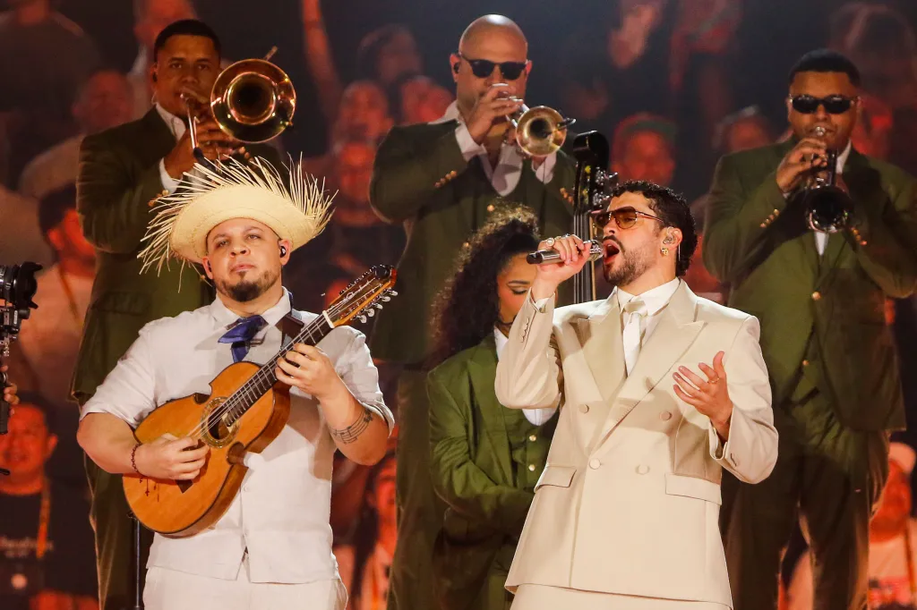 Bad Bunny performs in Medellin during his world tour, singing into a microphone with his band playing instruments.